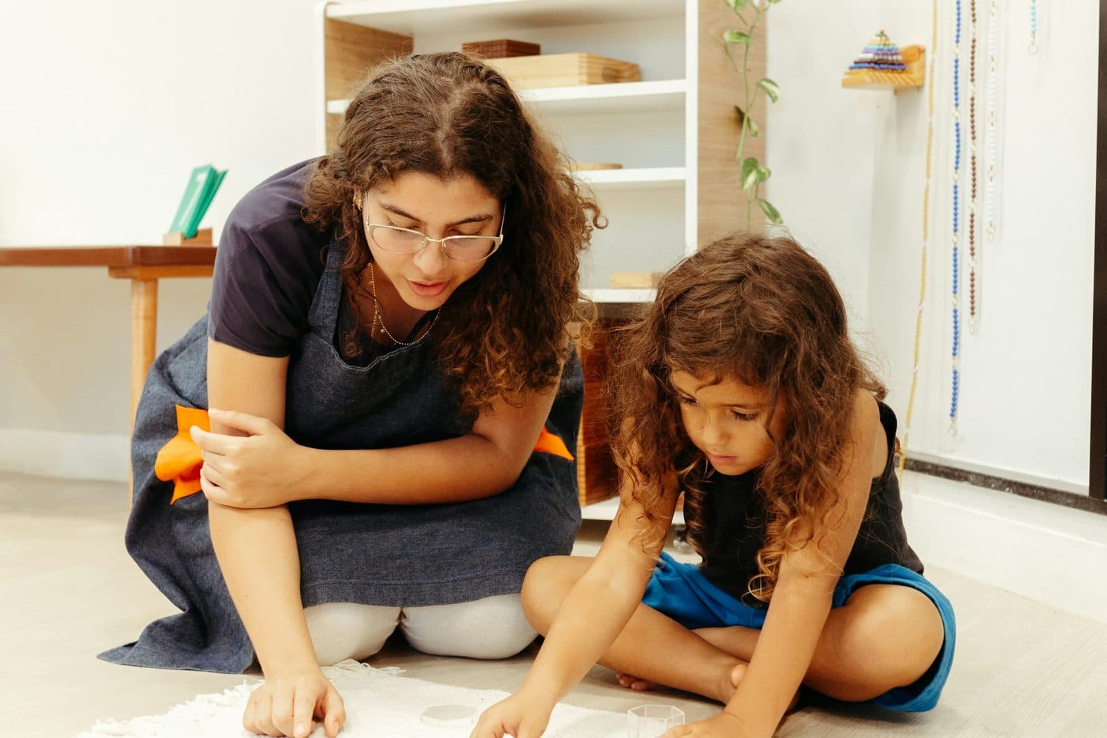 A teacher aide working one-to-one with a young learner on the classroom floor